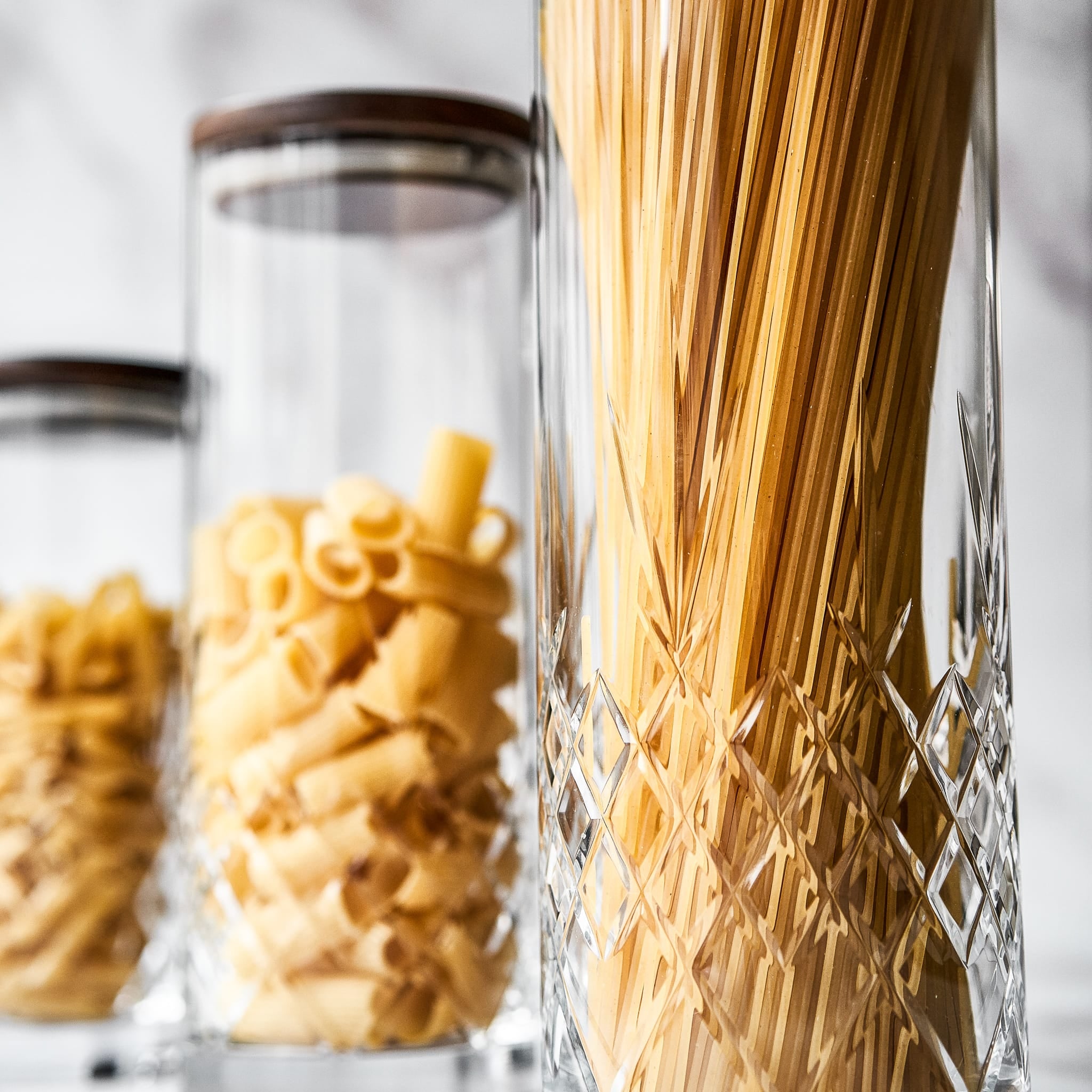 Klar glasskrukke med fasettslipt diamantmønster fylt med tørr pasta til interiør og oppbevaring.