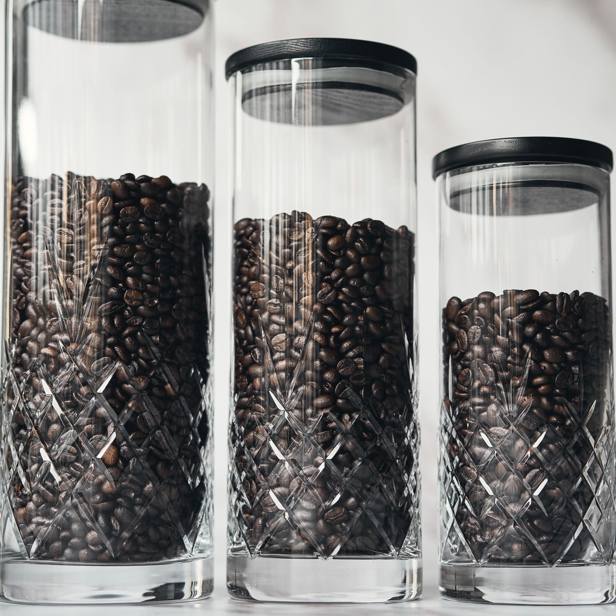 Trehyllet lokk i mørk ask på klart glass med ristede kaffebønner, skandinavisk interiør og funksjonelt design.