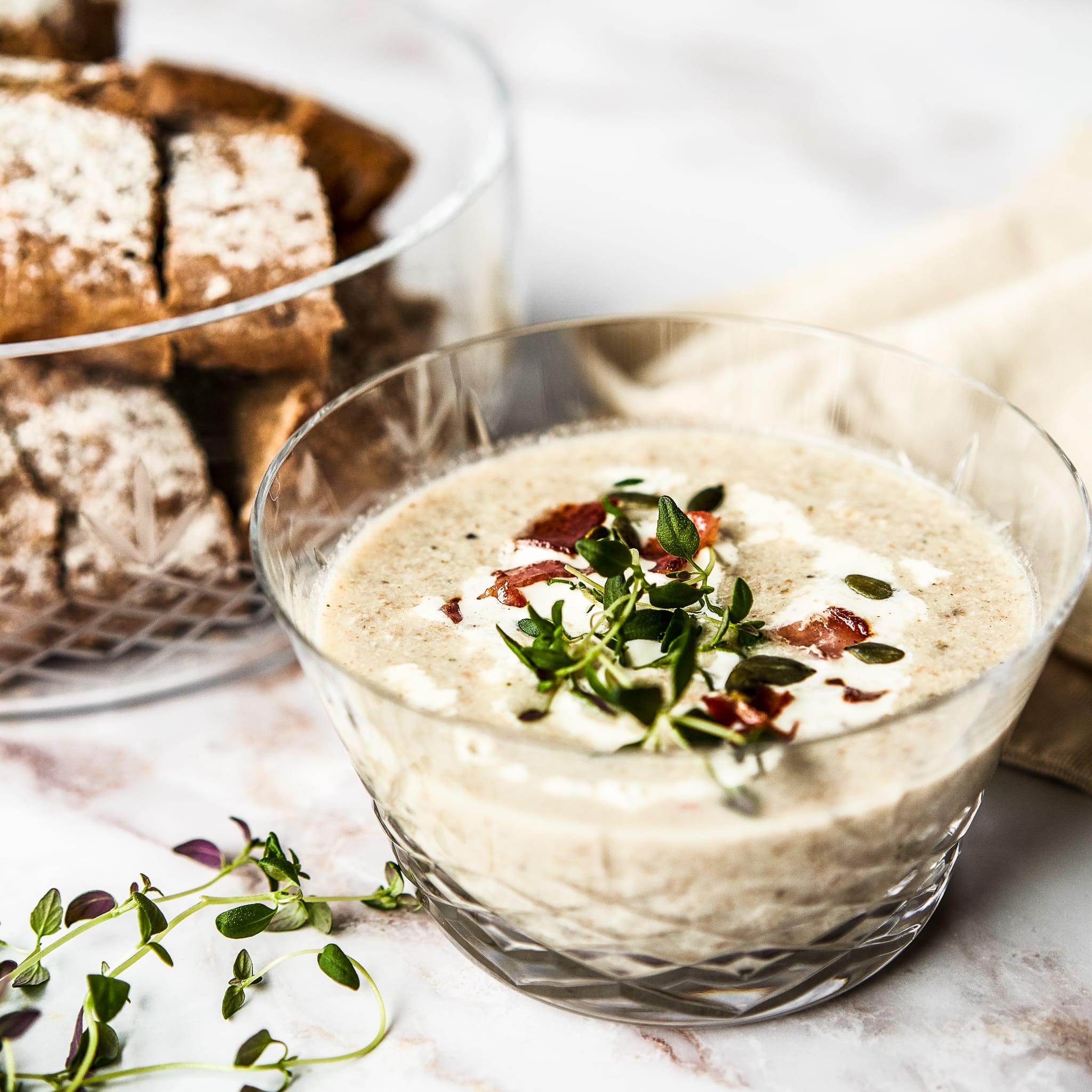 Klar Crispy-skål med suppe, topping av friske urter, plassert på bord med brød i bakgrunnen.