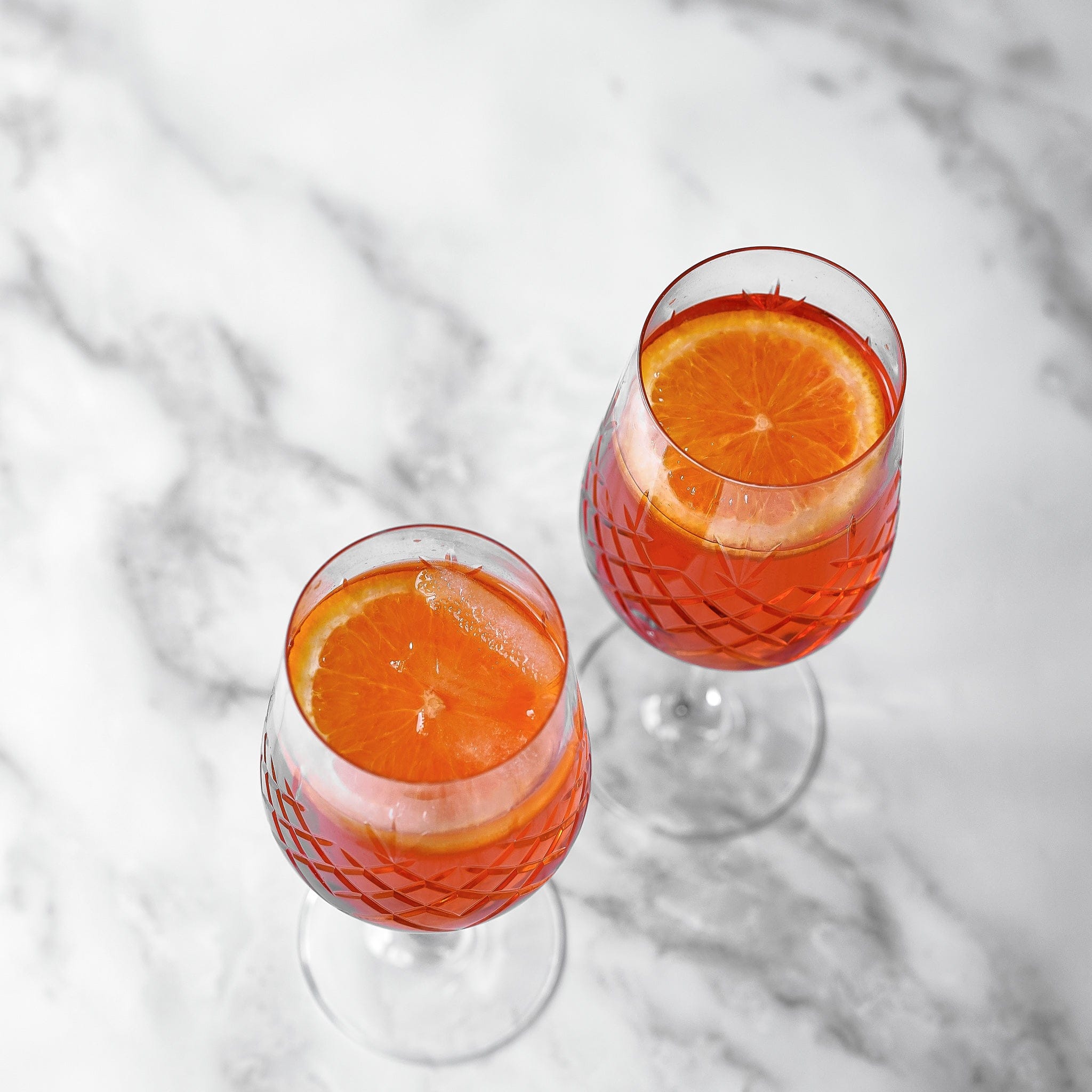 To vinglass med diamantmønster fylt med rødvin og appelsinskiver på marmorbord, skandinavisk design.