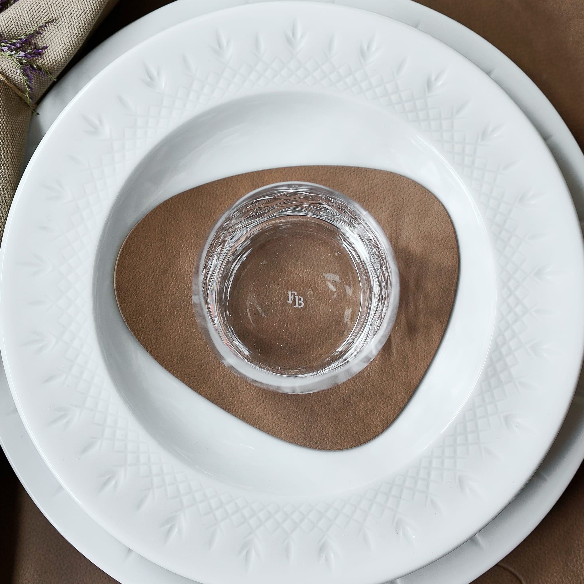Hvitt porselensfat med rillet mønster og klart glass med initialer på brunt underlag, skandinavisk design