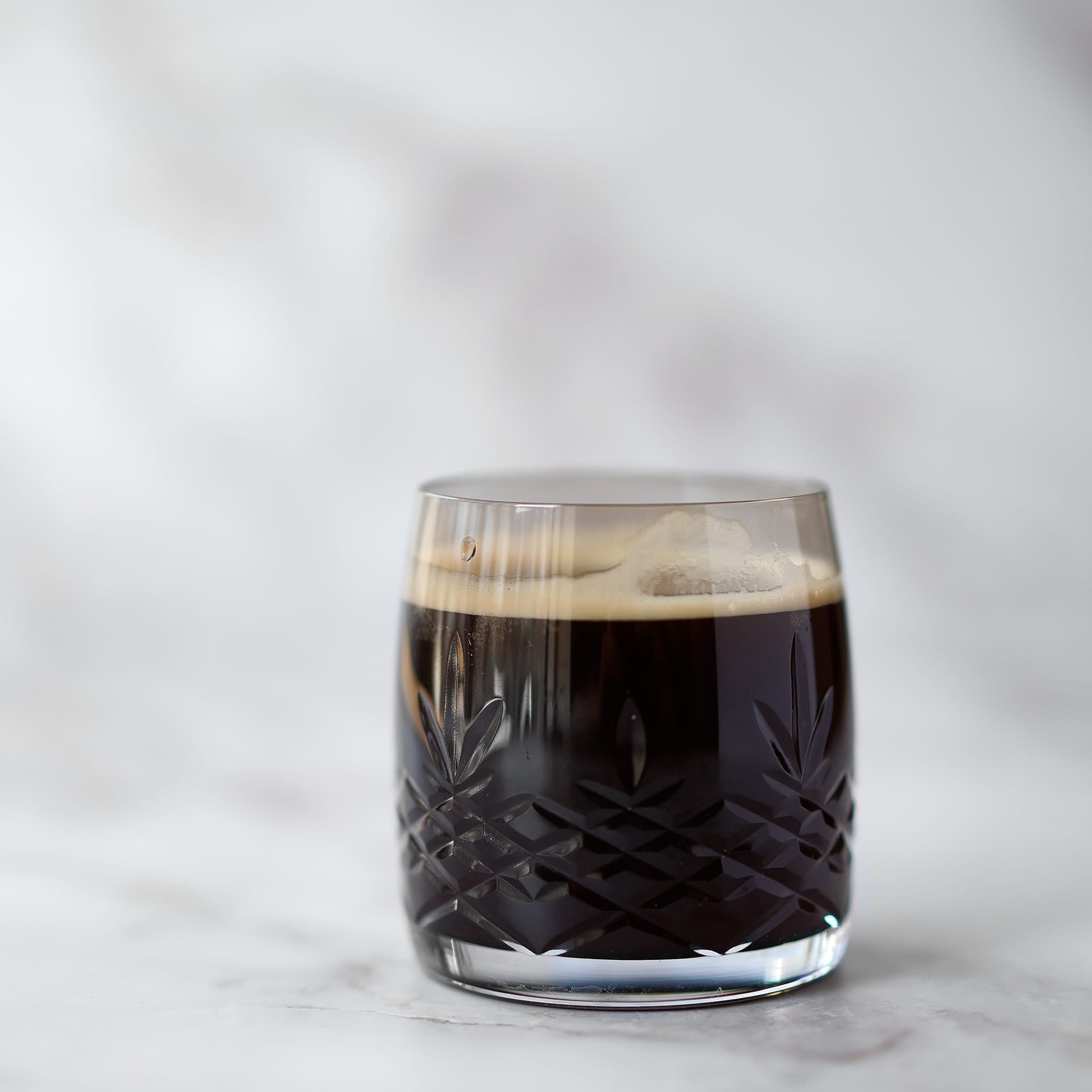 Fasettslipt krystallglass i brun copal med skandinavisk design fylt med kaffe på marmorflate.