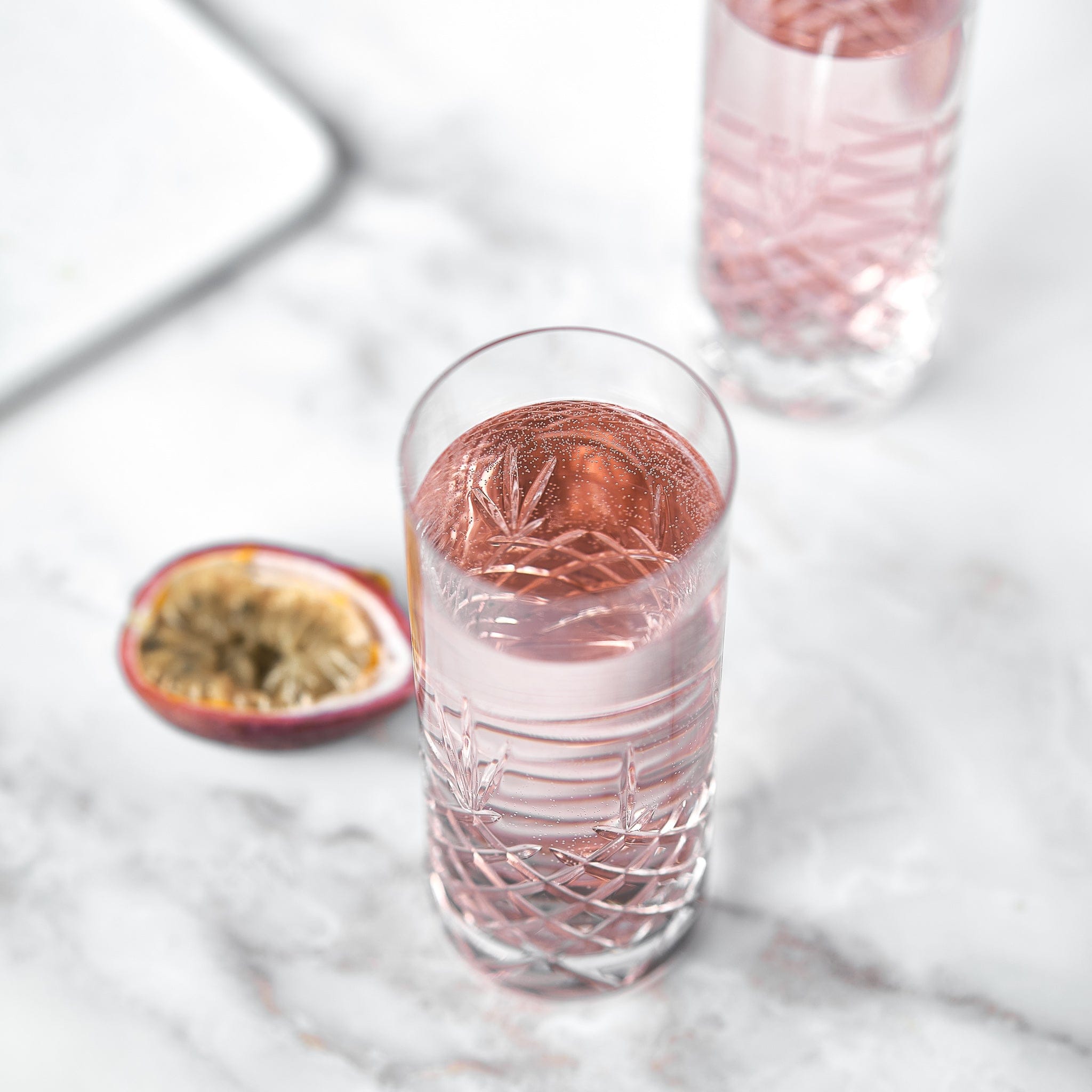 Høyt krystallglass med fasettslipt mønster fylt med rosa drikke på marmorbord, skandinavisk design.