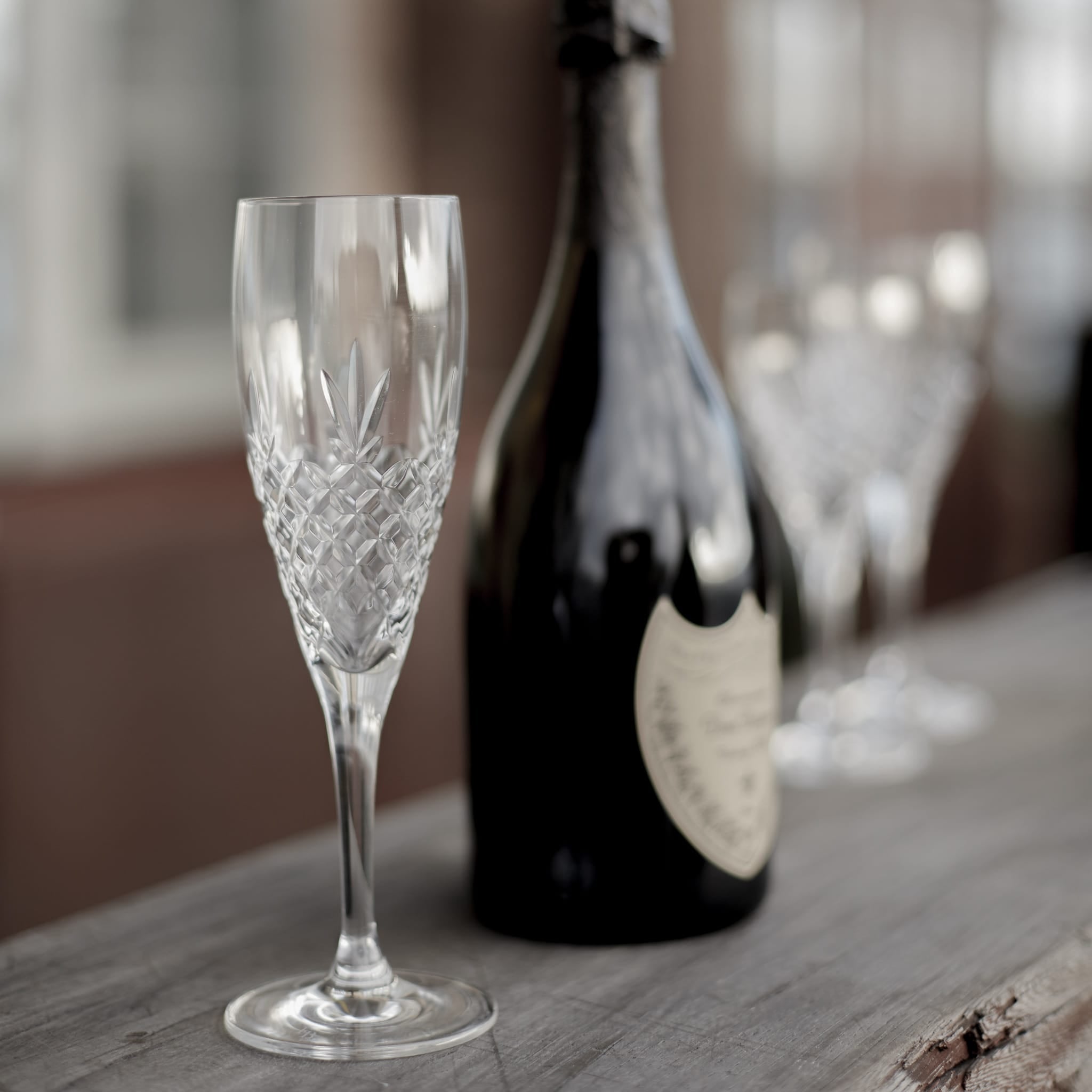 Klart krystallglass med diamantmønster i skandinavisk design ved siden av en mørk champagneflaske