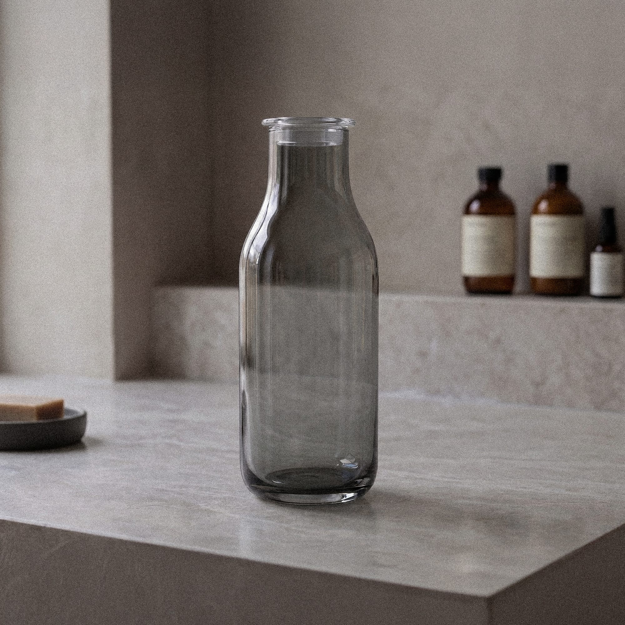 Røykfarget glasskaraffel med minimalistisk skandinavisk design fra Frederik Bagger på nøytral steinbenk.